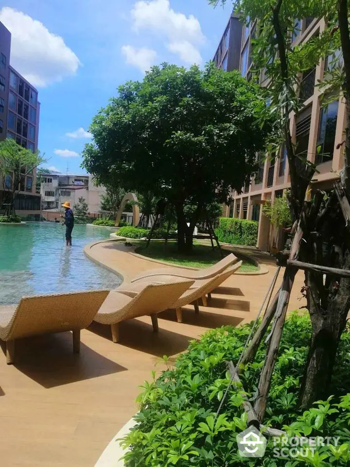 Luxurious poolside view with sun loungers and lush greenery in modern residential complex.