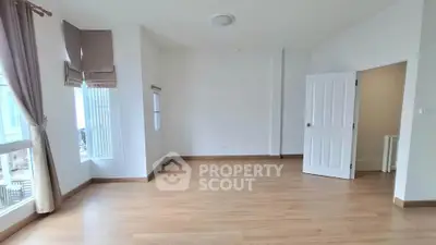 Spacious empty room with wooden flooring and large windows, perfect for customization.