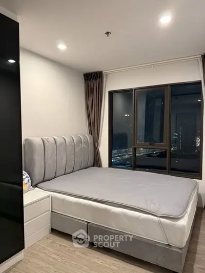 Modern bedroom with city view, featuring a plush bed and large window for natural light.