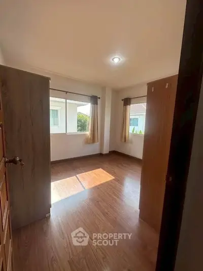 Bright bedroom with wooden flooring and large windows for natural light.