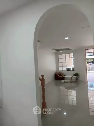 Spacious modern living room with glossy floors and archway entrance, featuring a cozy seating area and large window.