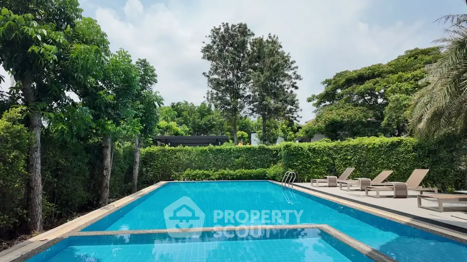 Luxurious outdoor pool surrounded by lush greenery and sun loungers, perfect for relaxation.