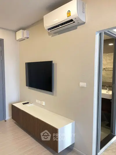 Modern living room with wall-mounted TV and air conditioning unit, sleek design and neutral tones.