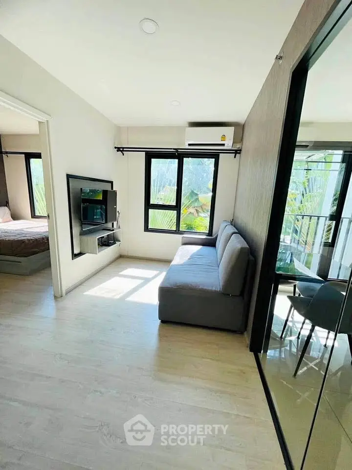 Bright modern living room with large windows and cozy sofa, adjacent to a stylish bedroom.