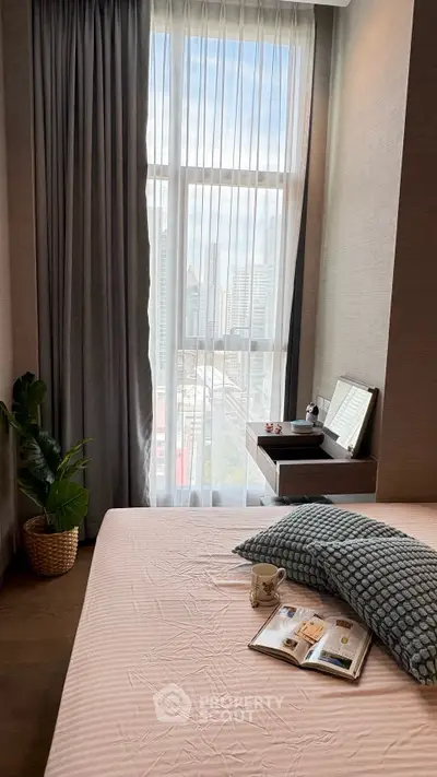 Cozy bedroom with large window offering city view, featuring stylish decor and natural light.