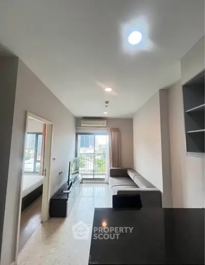 Modern living room with balcony view in a high-rise apartment, featuring sleek furniture and natural light.