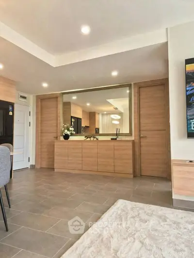 Modern living room with sleek wooden cabinetry and large mirror, featuring neutral tones and elegant decor.