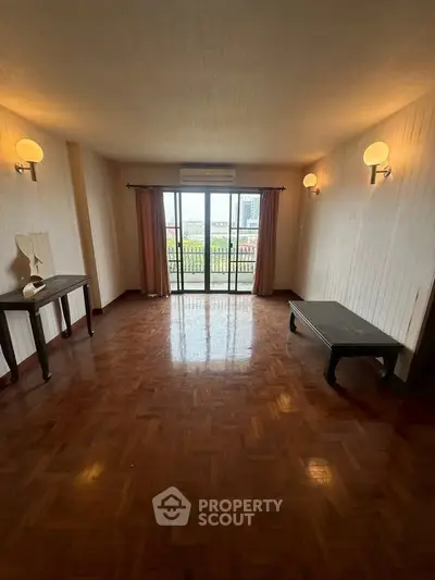 Spacious living room with parquet flooring and large windows opening to a balcony.