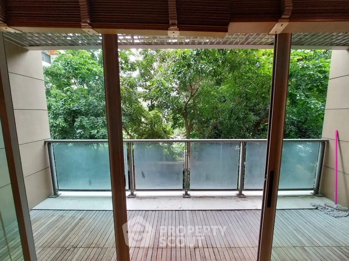 Spacious balcony with lush green view through sliding glass doors.