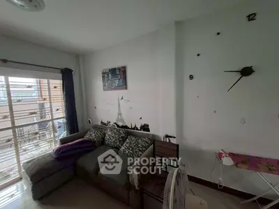 Cozy living room with modern decor and wall clock, featuring a comfortable sofa and balcony access.