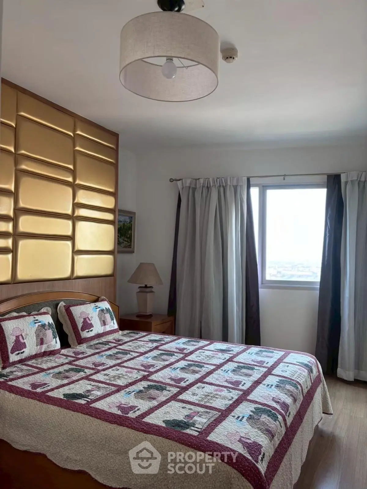 Cozy bedroom with stylish quilt and elegant curtains, featuring a modern light fixture and a scenic window view.