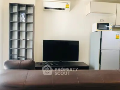 Modern living room with TV, air conditioning, and kitchen appliances in a cozy apartment.