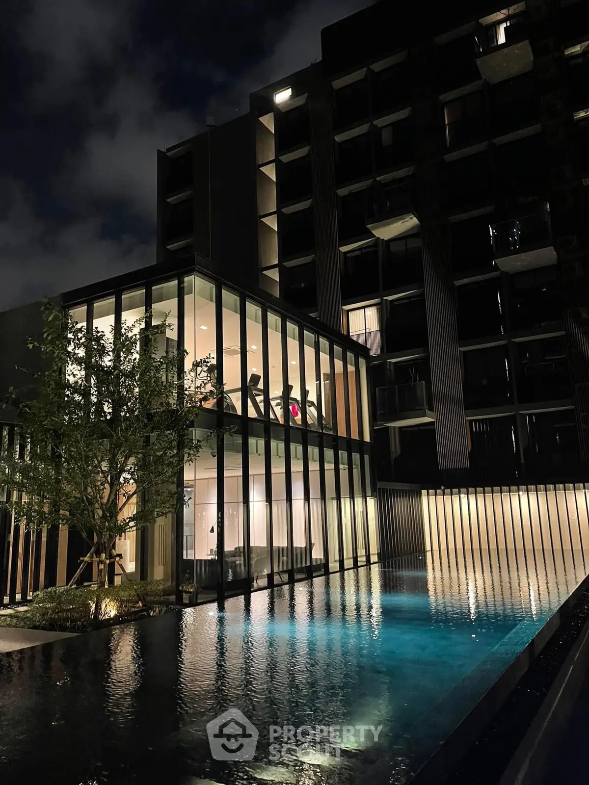 Luxurious modern building with illuminated glass facade and serene pool at night, perfect for upscale living.