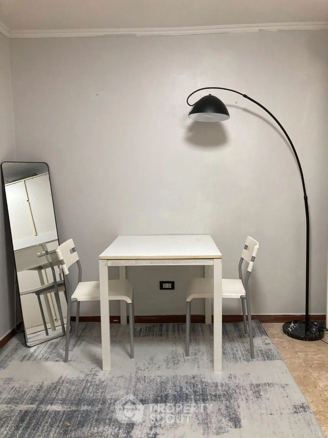 Minimalist dining area with white table, chairs, and floor lamp in modern apartment.