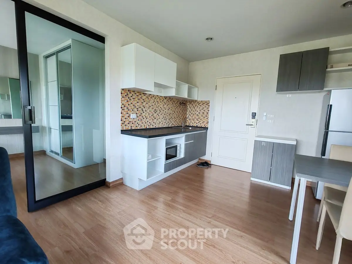 Modern apartment interior with sleek kitchen and dining area, featuring wood flooring and stylish cabinetry.