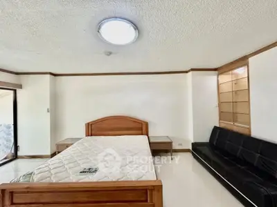 Spacious bedroom with wooden bed frame and modern sofa, ideal for comfort and relaxation.