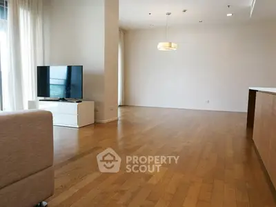 Spacious modern living room with hardwood floors and natural light, featuring a sleek TV setup.