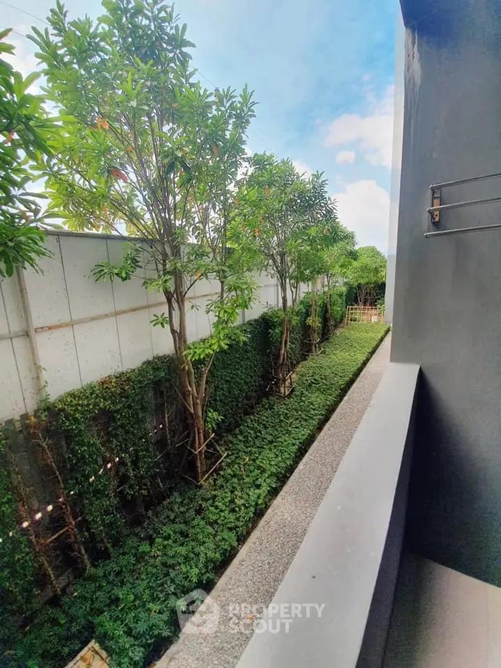 Charming garden view from a modern balcony with lush greenery and clear blue sky.