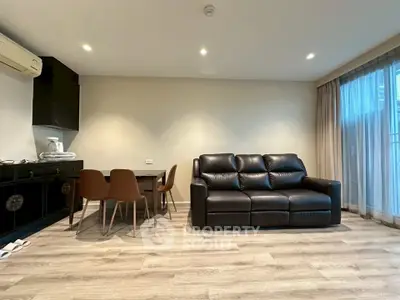 Modern living room with sleek black leather sofa and dining area, featuring stylish wood flooring and natural light.