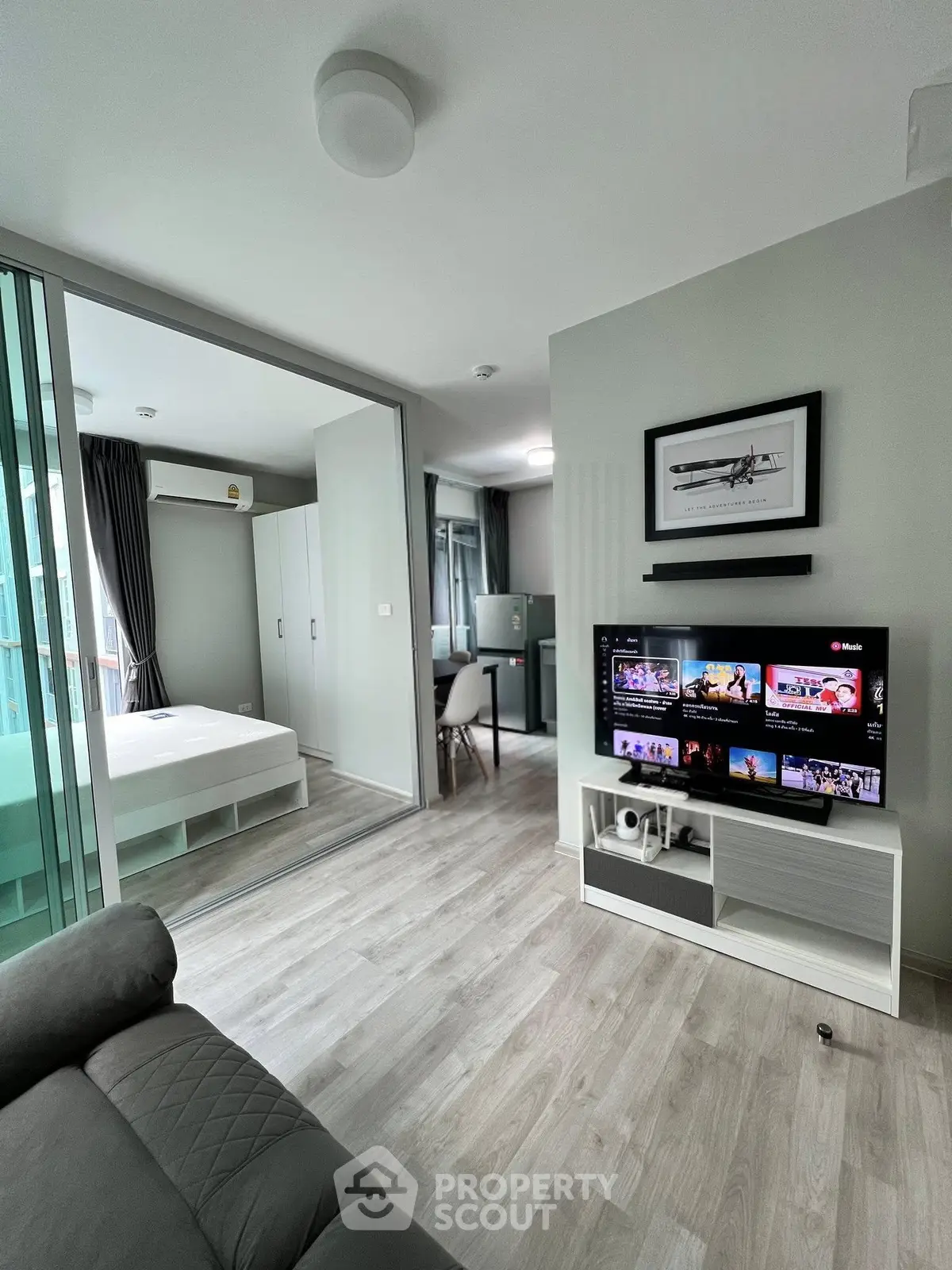 Modern apartment interior with open living room and bedroom, featuring sleek furniture and a wall-mounted TV.