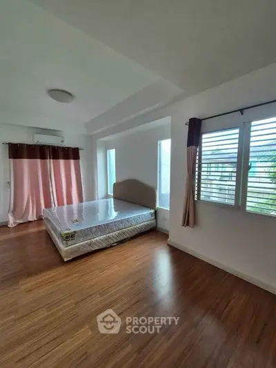 Spacious bedroom with large windows and wooden flooring in modern apartment