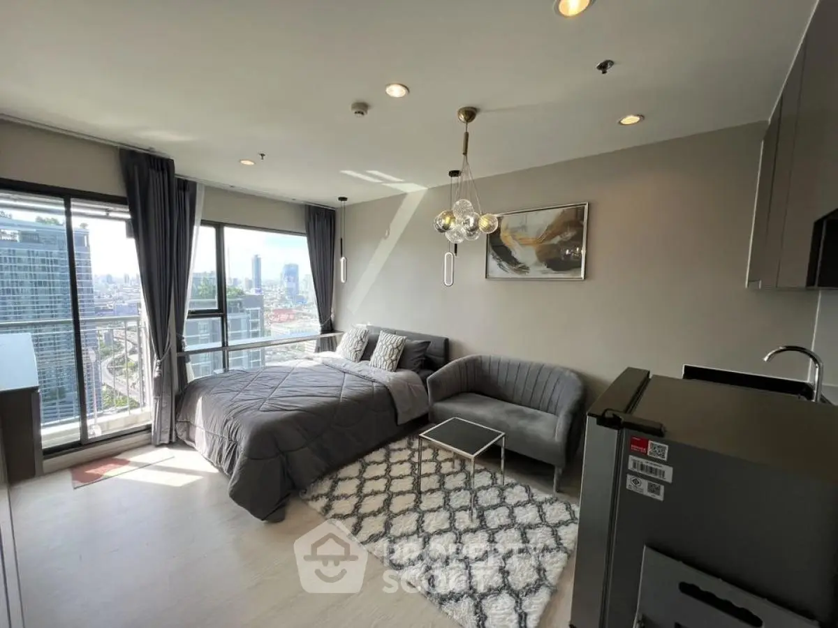 Modern studio apartment with city view, featuring a cozy bed, stylish sofa, and sleek kitchenette.