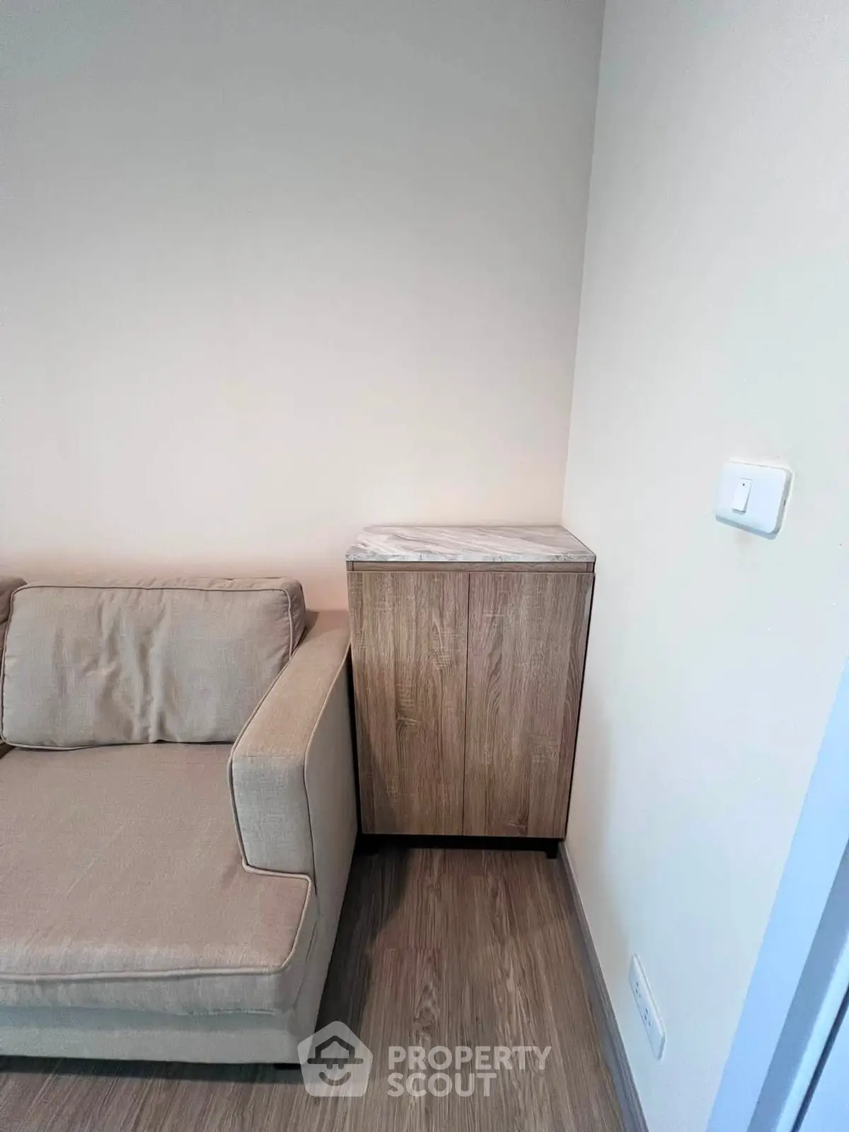 Modern living room corner with beige sofa and wooden cabinet on sleek flooring.