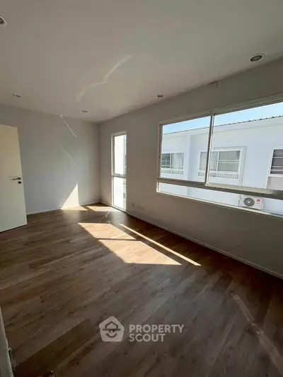 Spacious sunlit room with large windows and wooden flooring, perfect for a modern living space.