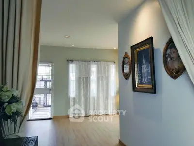 Elegant living room with wooden flooring and decorative wall art, featuring large windows with sheer curtains.