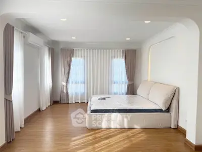 Spacious bedroom with elegant curtains and natural light, featuring a comfortable bed and wooden flooring.