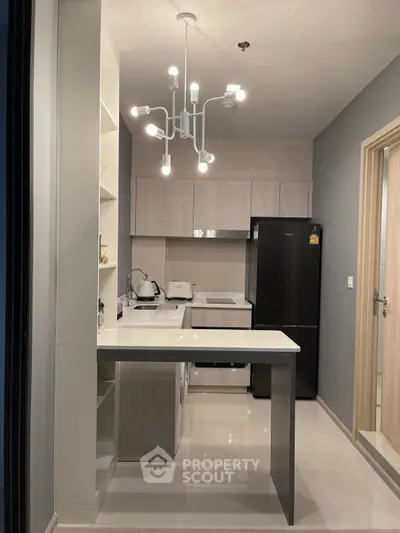 Modern kitchen with sleek design, featuring black fridge, white countertops, and stylish lighting.