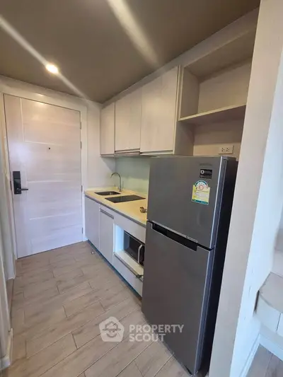 Modern compact kitchen with sleek cabinets and stainless steel fridge in a stylish apartment.