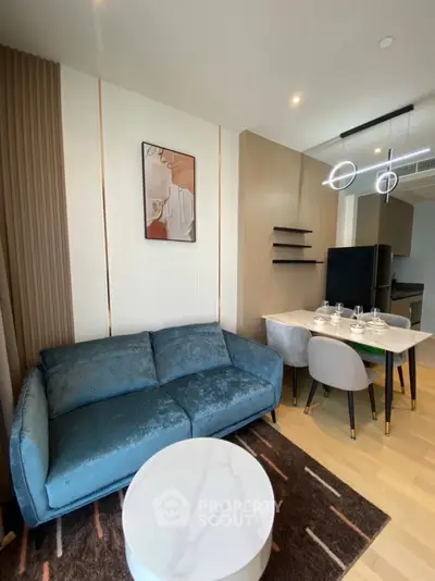 Modern living room with stylish decor and open kitchen layout, featuring a cozy blue sofa and elegant dining area.