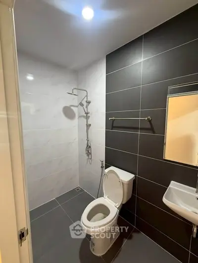 Modern bathroom with sleek black and white tiles, featuring a shower, toilet, and sink.