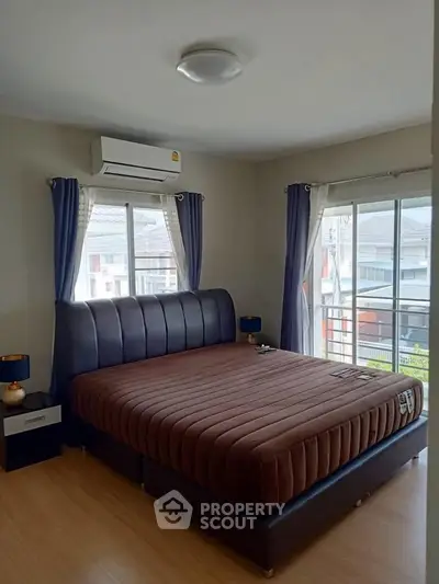 Spacious bedroom with large windows and modern furnishings in a well-lit apartment.