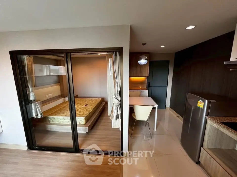 Modern studio apartment with glass partition, cozy bedroom, and sleek kitchen area.