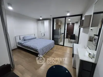 Modern studio apartment with sleek design and wooden flooring, featuring a cozy bed and compact kitchen area.