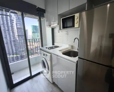 Modern compact kitchen with balcony view, featuring washing machine, microwave, and stainless steel fridge.