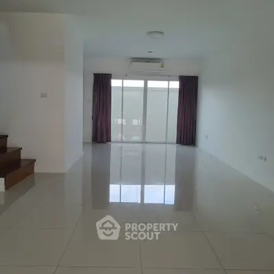 Spacious empty living room with glossy tiled floors and large window for natural light.