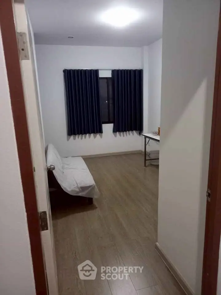 Minimalist bedroom with wooden flooring and dark curtains, perfect for a cozy retreat.