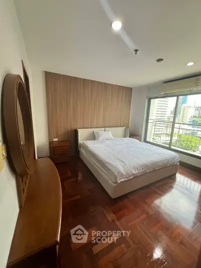 Spacious bedroom with wooden flooring and city view balcony in modern apartment