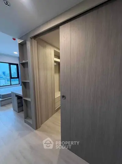 Modern bedroom with sliding door and city view, featuring sleek built-in storage and natural light.