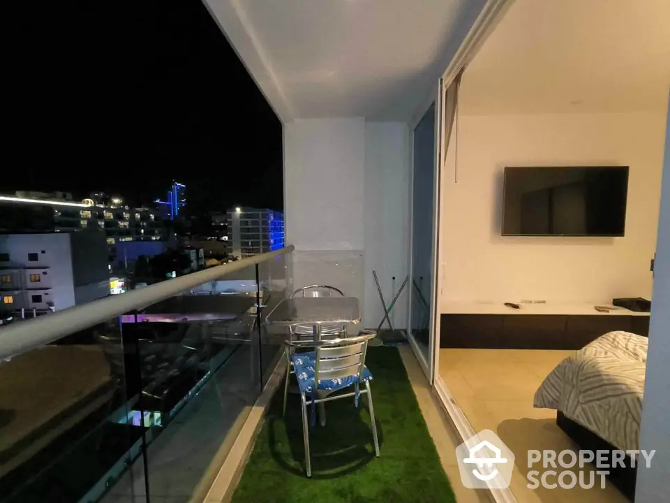 Modern apartment balcony with night city view and cozy seating area.