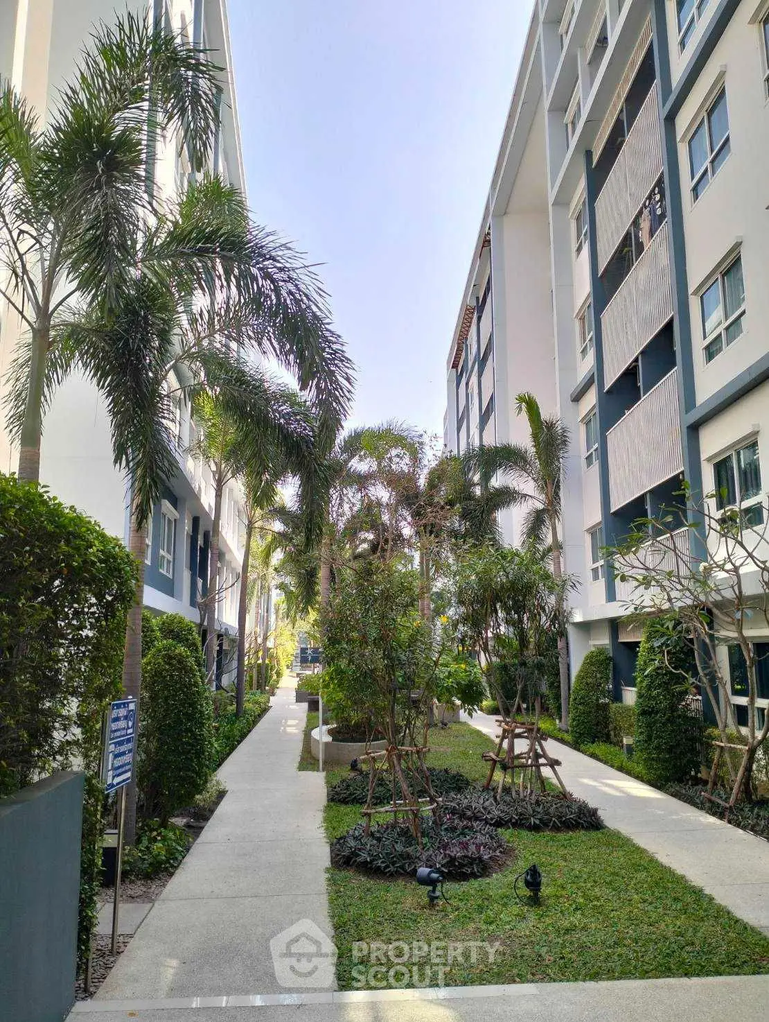 Modern apartment complex with lush garden and palm trees, offering a serene urban living environment.