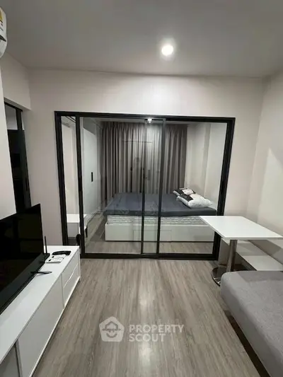Modern studio apartment with glass partition, cozy bed, and sleek flooring.