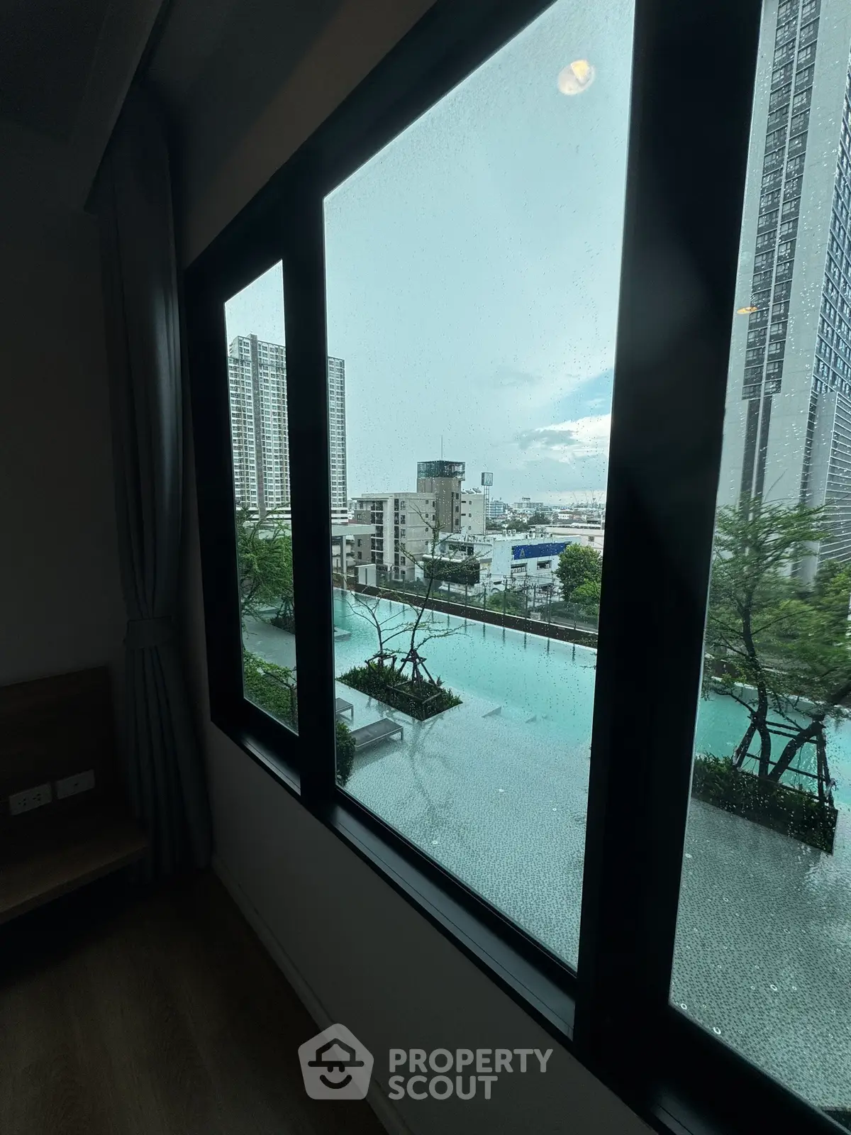 Stunning cityscape view from a high-rise apartment window overlooking a serene pool area.
