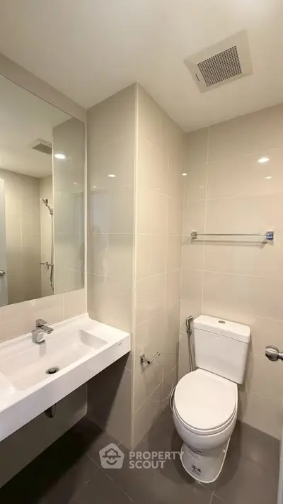 Modern bathroom with sleek fixtures and neutral tiles, featuring a spacious mirror and contemporary design.