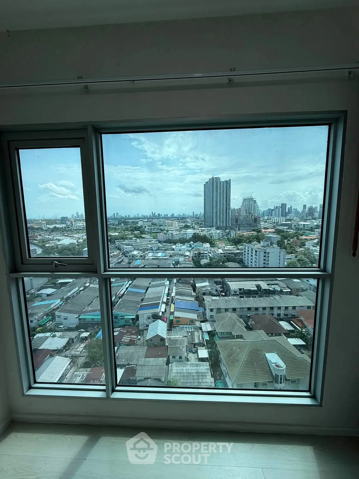 Stunning cityscape view from a high-rise apartment window, showcasing urban skyline and residential rooftops.