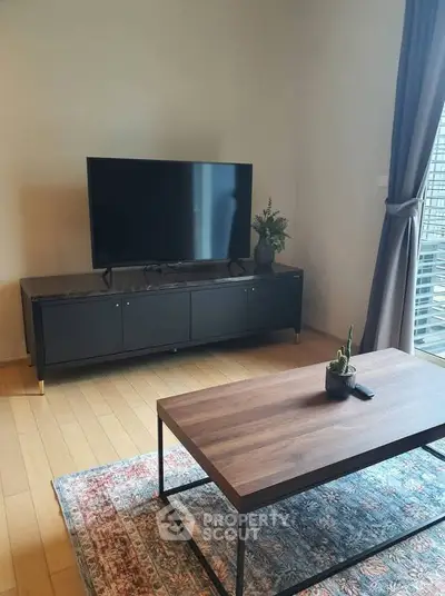 Modern living room with sleek TV stand, large flat-screen TV, and stylish coffee table on a patterned rug.