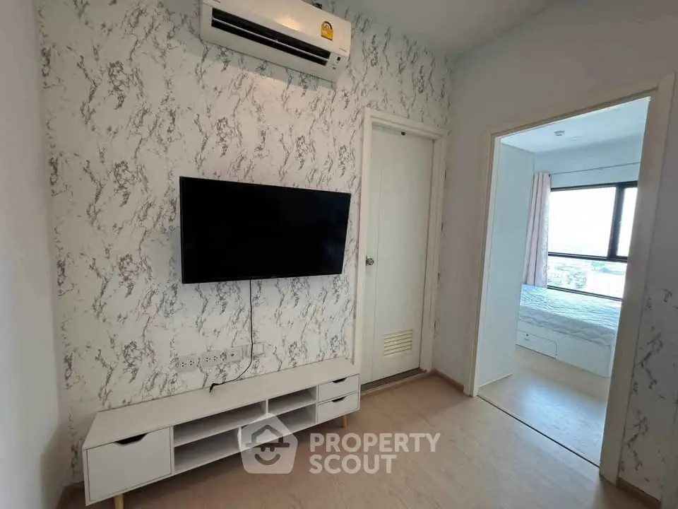 Modern living room with wall-mounted TV and air conditioning, leading to a bright bedroom with large window.